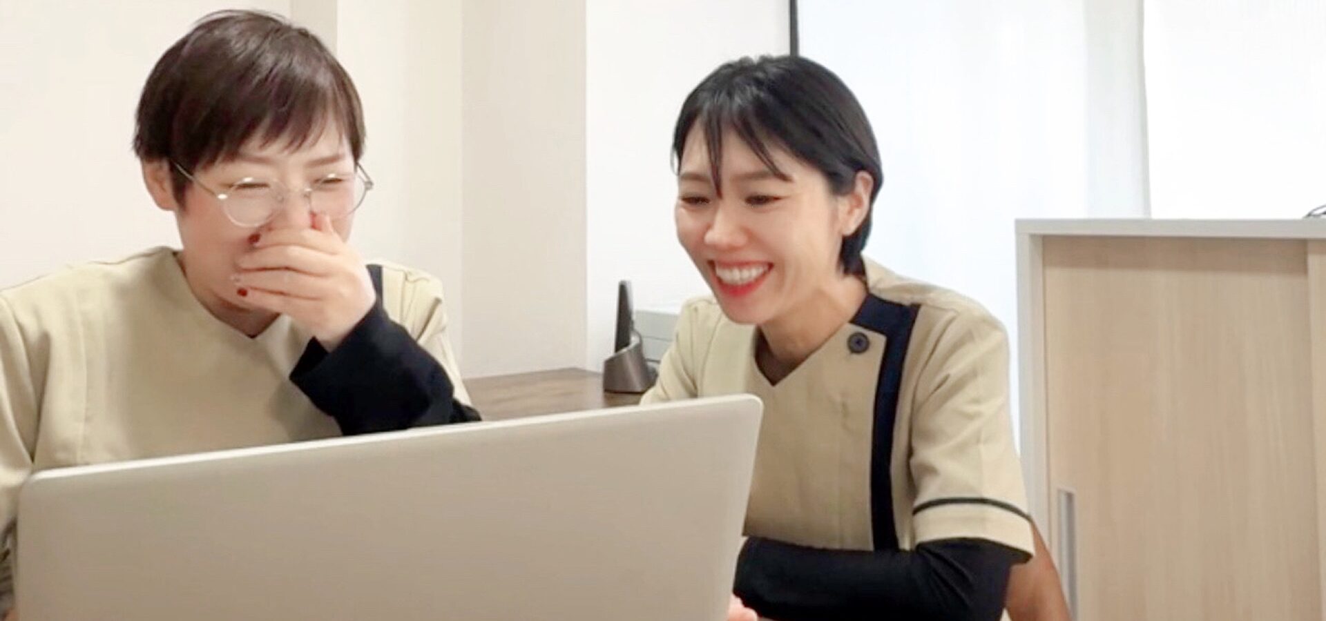 訪問看護ステーションすこやかのスタッフが笑顔でパソコンを覗き込む様子